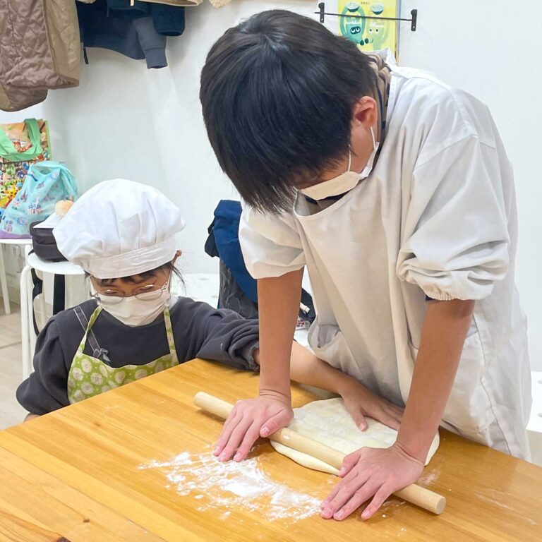 妹が見守る中、お兄ちゃんが麺棒でうどん生地を大きく伸ばしている場面 手打うどん作り体験教室 2025年10月 2.jpg – イリコスキー製麺所
