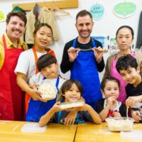 参加者が切った麺を手に、教室内で記念撮影している様子 手打ちうどん作り体験教室 2025年12月 A6407386-1.jpg – イリコスキー製麺所