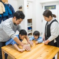 家族みんなで協力して、麺棒を使ってうどん生地を伸ばしている様子。 Family members working together to roll out the udon dough using a rolling pin. 手打ちうどん作り体験教室 2026年1月 3.jpg – イリコスキー製麺所