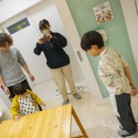 テーブルで作業する子供をスマートフォンで撮影する女性。A woman taking a photo of a child working at the table with her smartphone. 手打ちうどん作り体験教室 2026年1月 A6407796-1.jpg – イリコスキー製麺所