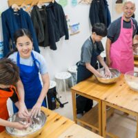 ボウルの中で粉と水を混ぜてうどんの生地作りをしている家族 A family mixing flour and water in bowls to make udon dough 手打ちうどん作り体験教室 2026年1月 A6408107-1.jpg – イリコスキー製麺所