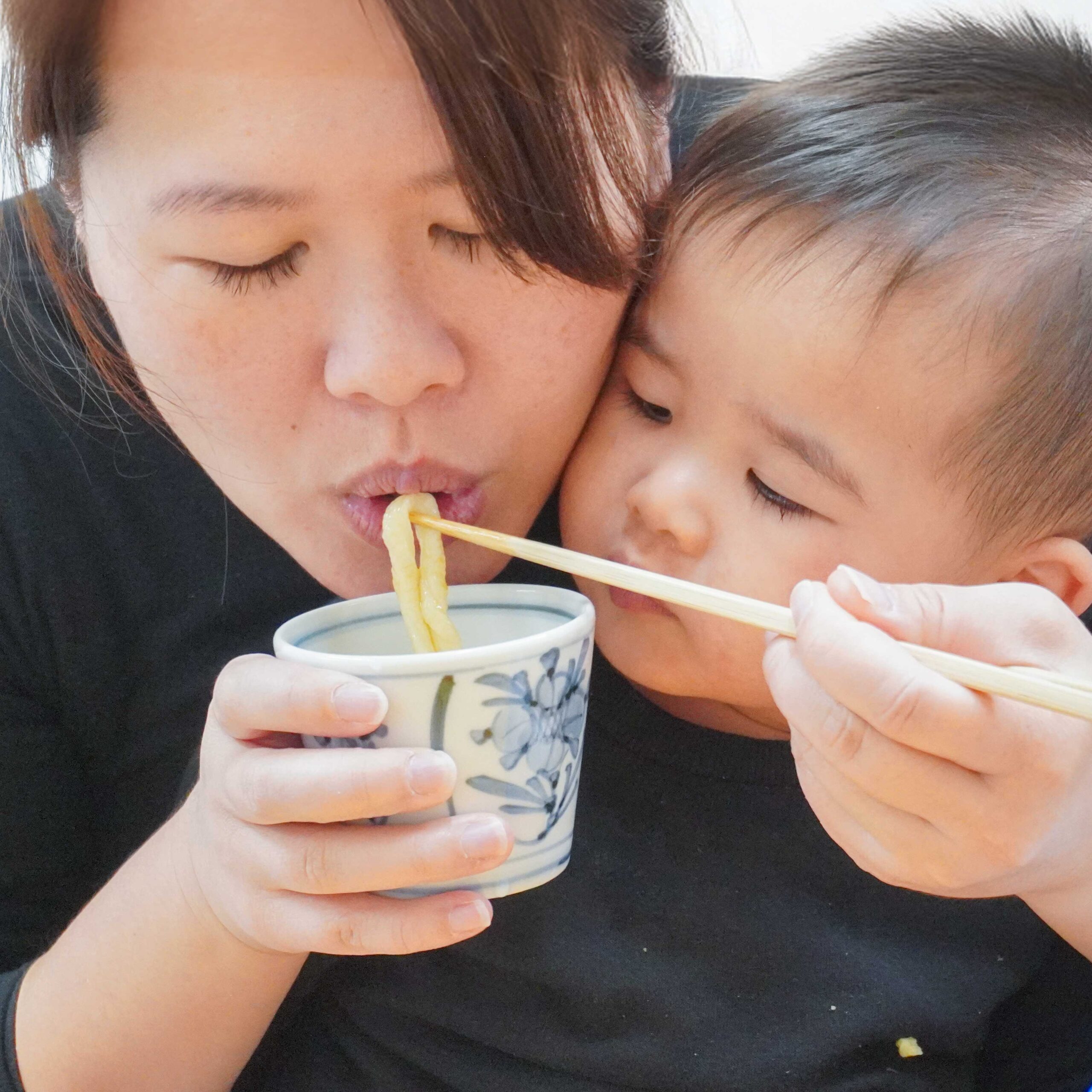 お母さんにうどんを冷ましてもらい、大きな口で食べる1歳半の男の子。 (A 1.5-year-old boy opening his mouth wide to eat udon noodles being cooled down by his mother.) 手打ちうどん作り体験教室 2026年1月 A6408310-1-scaled.jpg – イリコスキー製麺所