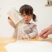 生地に打ち粉を丁寧にふりかける女の子。 / The little girl carefully sprinkling dusting flour over the dough. 手打ちうどん作り体験教室 2026年2月 A6408524-1-scaled.jpg – イリコスキー製麺所