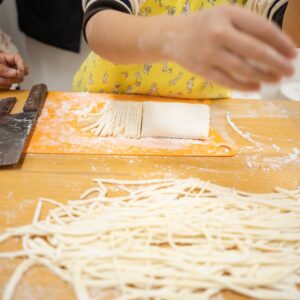 切りそろえた麺が広がり、包丁と生地が作業台に並ぶ仕上げの場面。 Freshly cut noodles spread across the table with a knife and dough on the work surface. 手打ちうどん作り体験教室 2026年2月 freshly-cut-udon-noodles-on-table.jpg – イリコスキー製麺所
