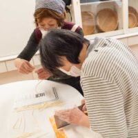 の女性が切ったうどんを確認しながら麺切りしている。A woman in a striped shirt cutting udon noodles on a
cutting board.