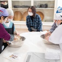 3人の女性がボウルの中で小麦粉と水を混ぜ合わせている。Participants mixing flour and water in large bowls at the
start of the udon-making process.