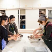 親子と女性がボウルの中でうどん生地を混ぜている。A mother-daughter pair and another participant mixing udon dough
in bowls.