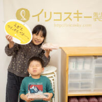 イリコスキー製麺所のバナーの前で、完成したうどんとフォトプロップスを持って記念撮影する子どもたち。 手打ちうどん作り体験教室 2026年3月 udon-class-kids-completed-noodles-iricosky-banner-1.jpg – イリコスキー製麺所
